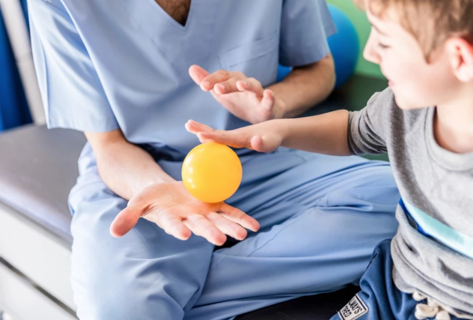 Dziecko bawiące się żółtą piłką na dłoni lekarza
